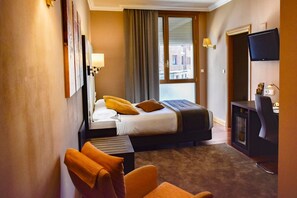 A hotel room with a bed, a desk, a chair, a television, and a window with curtains.