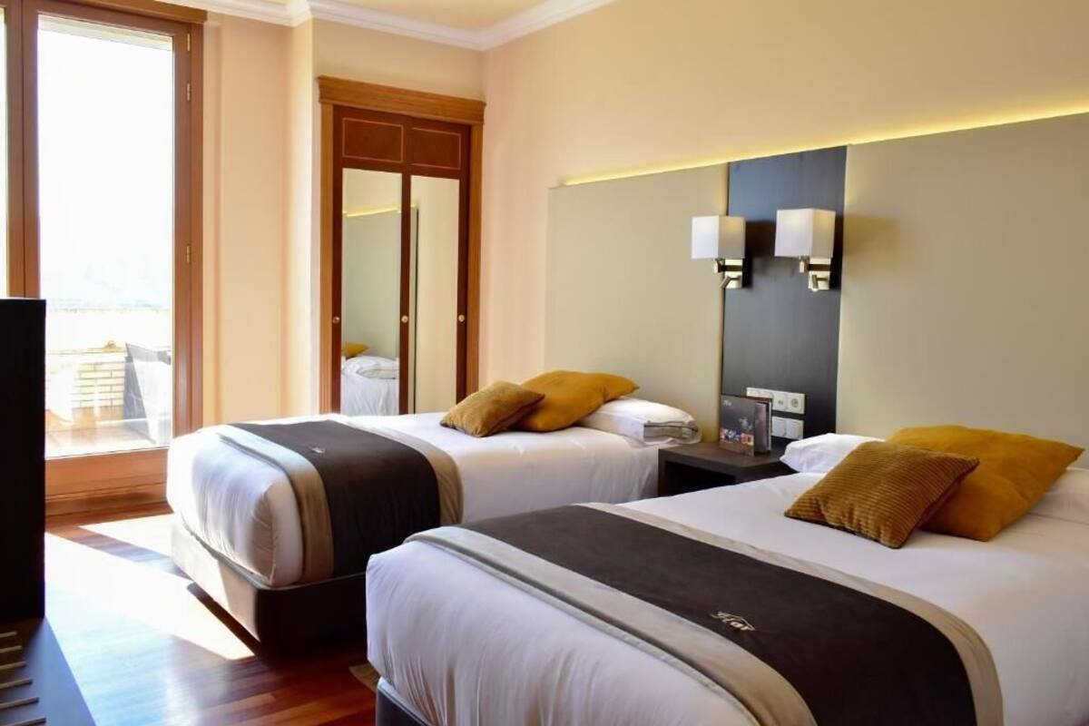 A hotel room with two beds, a large mirror, bedside lamps, and a view of the outdoors.