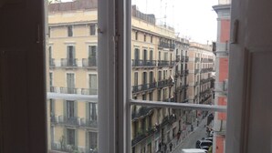 A view from a window overlooking a street with multi-story buildings, a clear sky, and a few parked vehicles. - Brustar Gòtic (Barcelona)