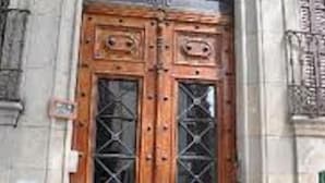 A double wooden door with glass panels and a metal grille, set in a stone building with an arched window above. - Brustar Gòtic (Barcelona)