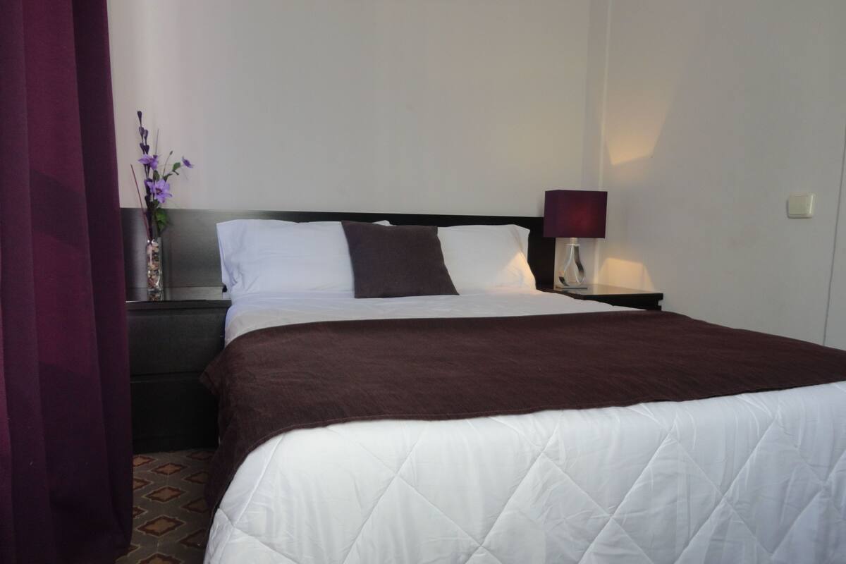 A hotel room with a large bed, a nightstand with a lamp, and a vase with flowers.