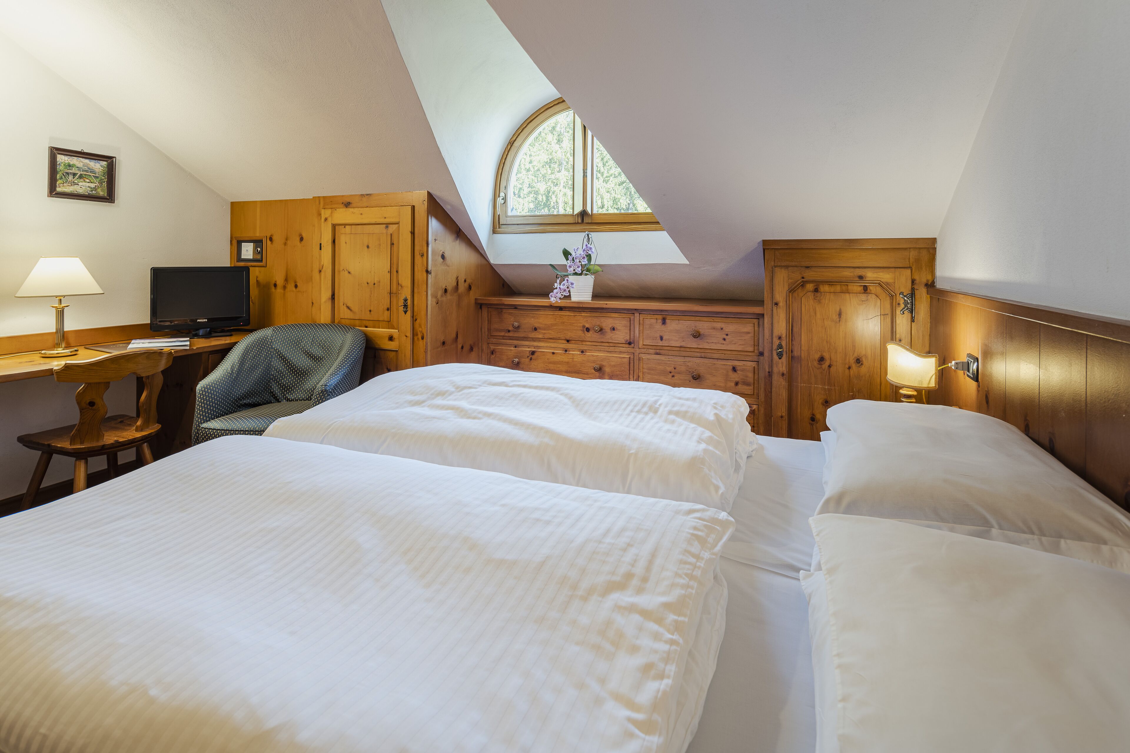 A bedroom with two beds, a desk, a chair, a TV, and a window.