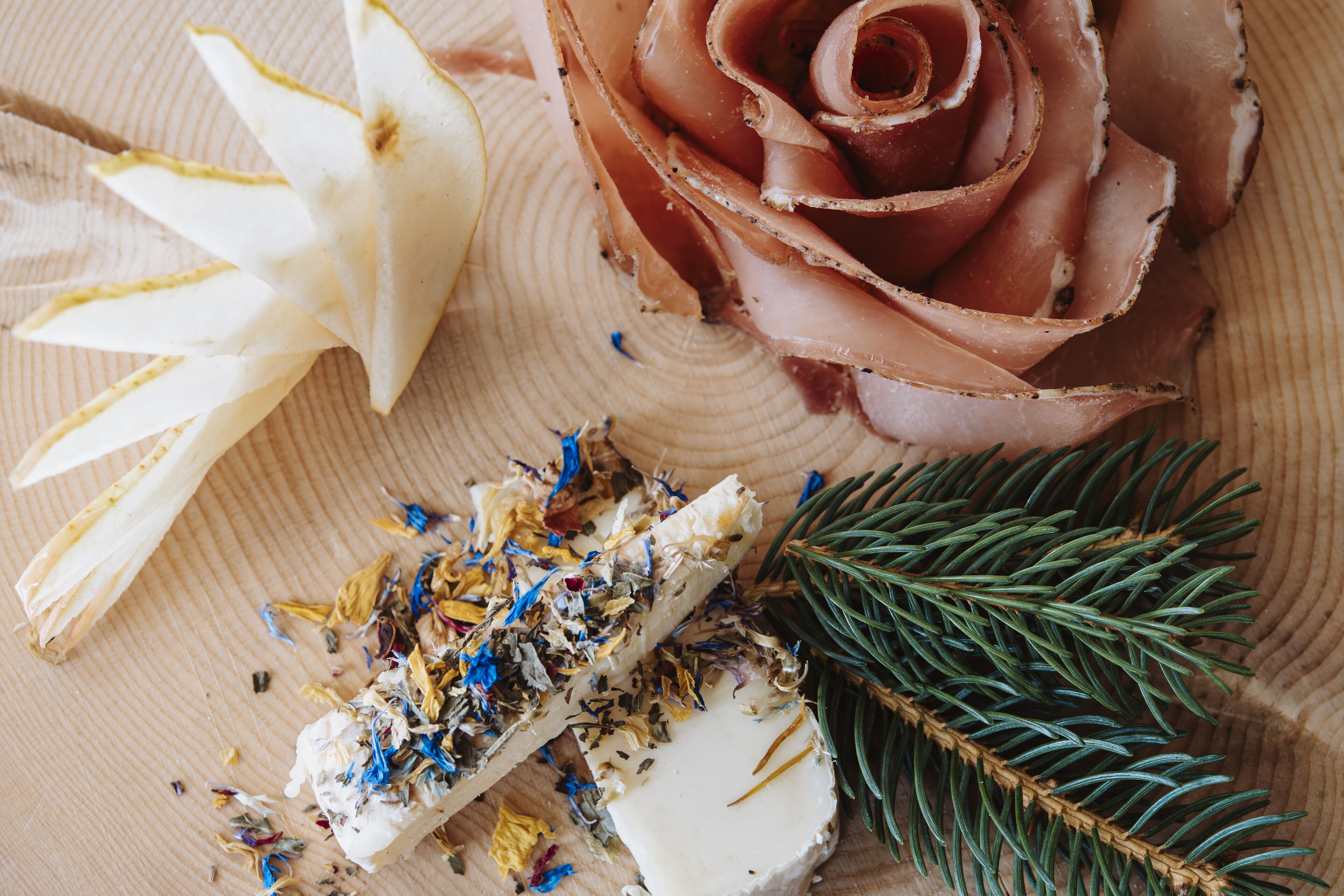 A wooden surface with a rose, a piece of meat, and a branch of pine.