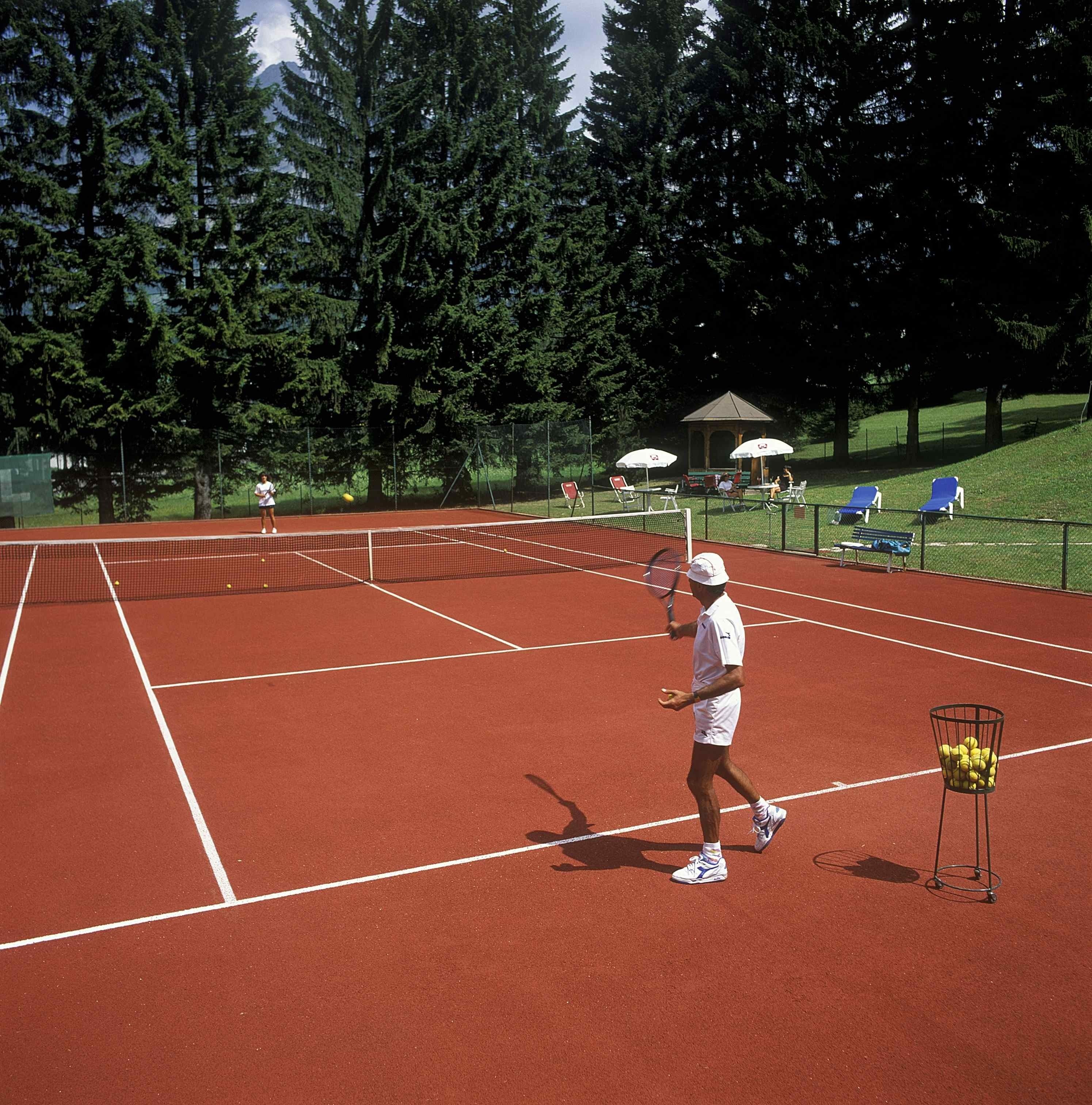 A tennis court with a net, surrounded by trees and a gazebo.