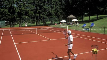 A tennis court with a net, surrounded by trees and a gazebo.