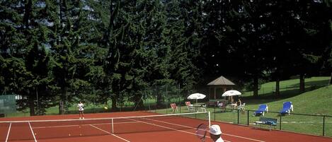 Pistes de tennis amb una xarxa, envoltades per arbres i un porxo.