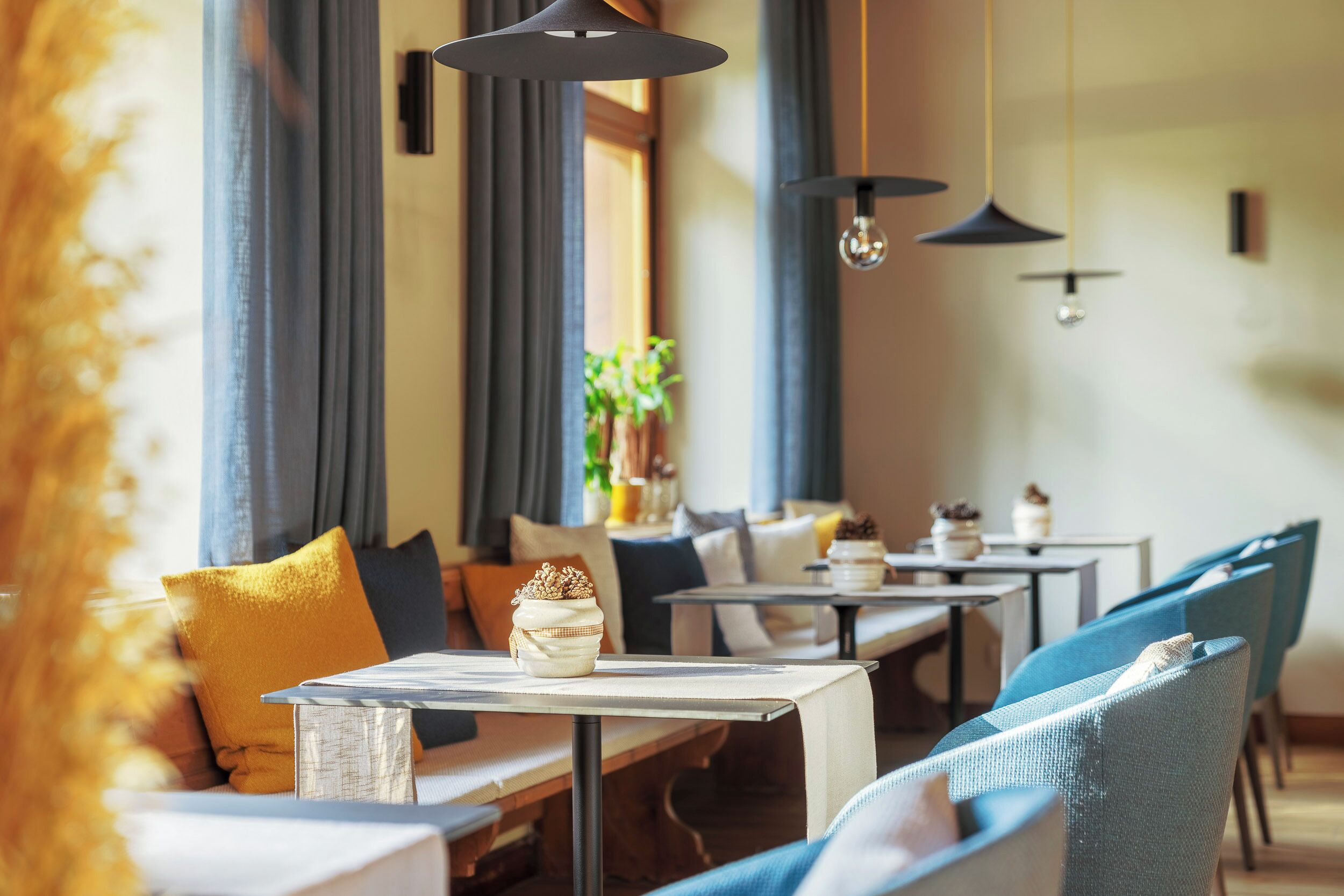 Un restaurante con mesas, sillas, una planta y lámparas colgantes.