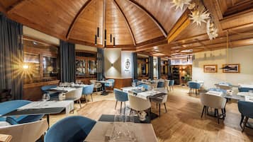A restaurant with wooden ceiling and walls, tables set with white tablecloths and blue chairs.