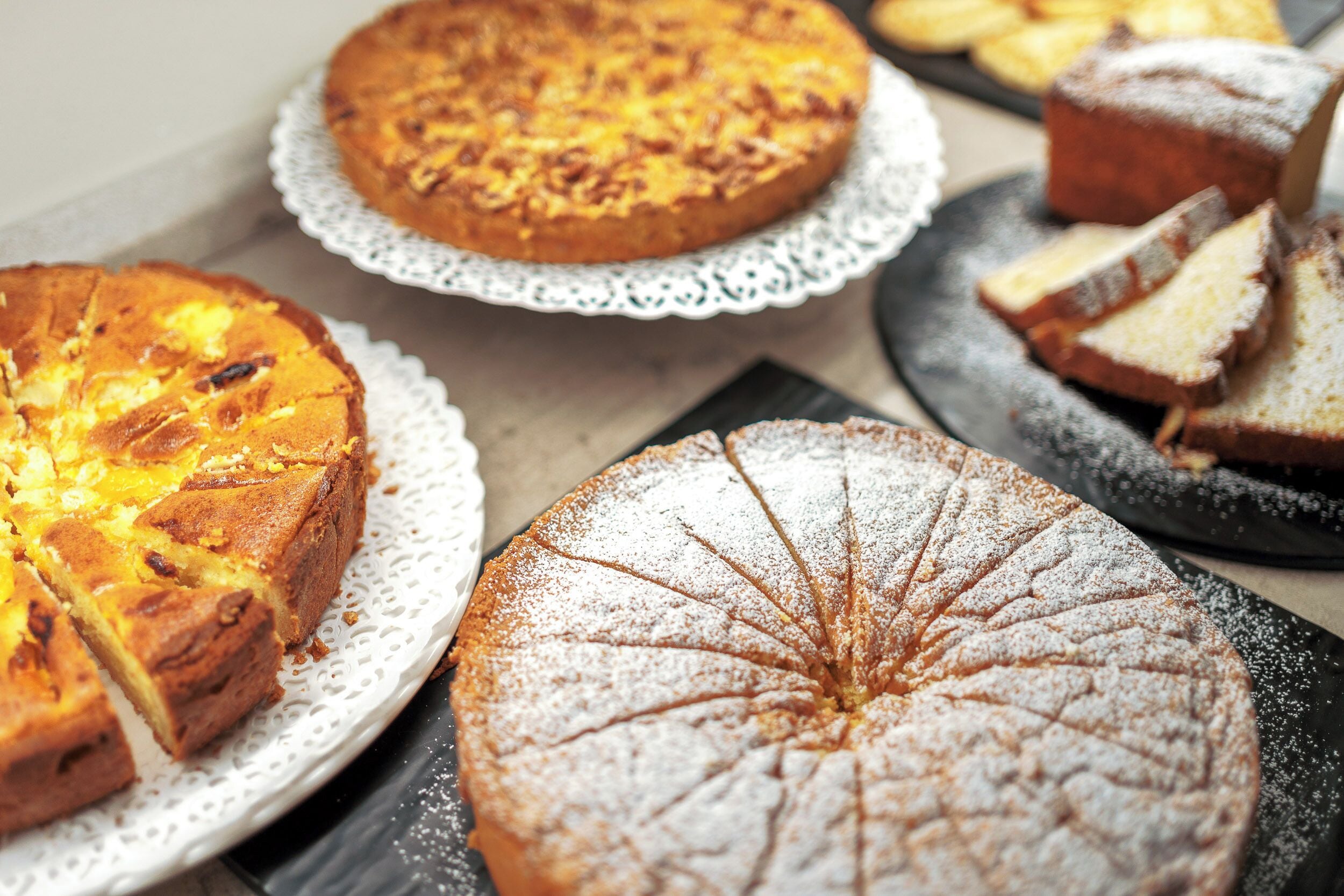 A variety of cakes on different plates, some with powdered sugar.