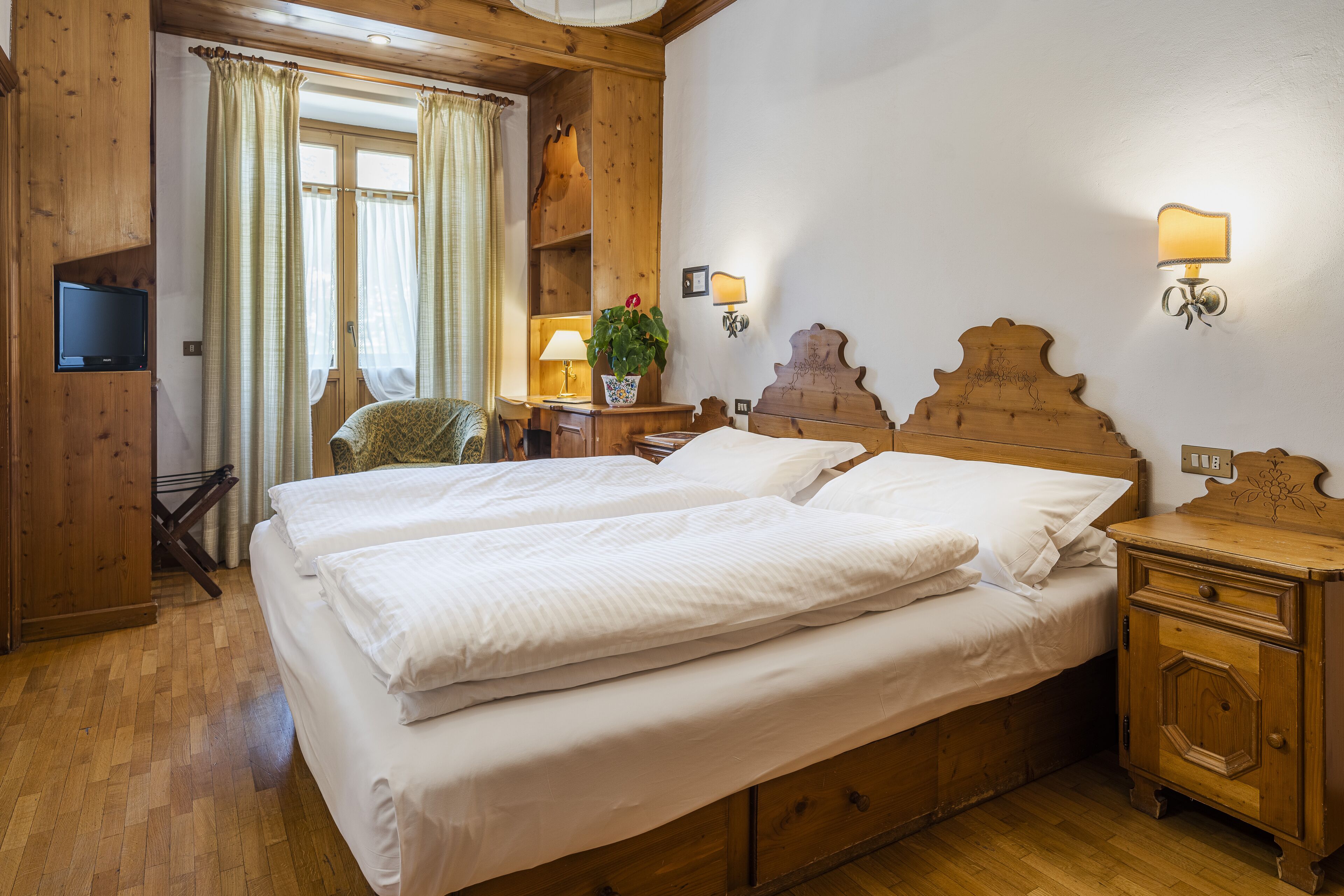 A wooden room with a bed, a TV mounted on the wall, a lamp, and a wooden cabinet.