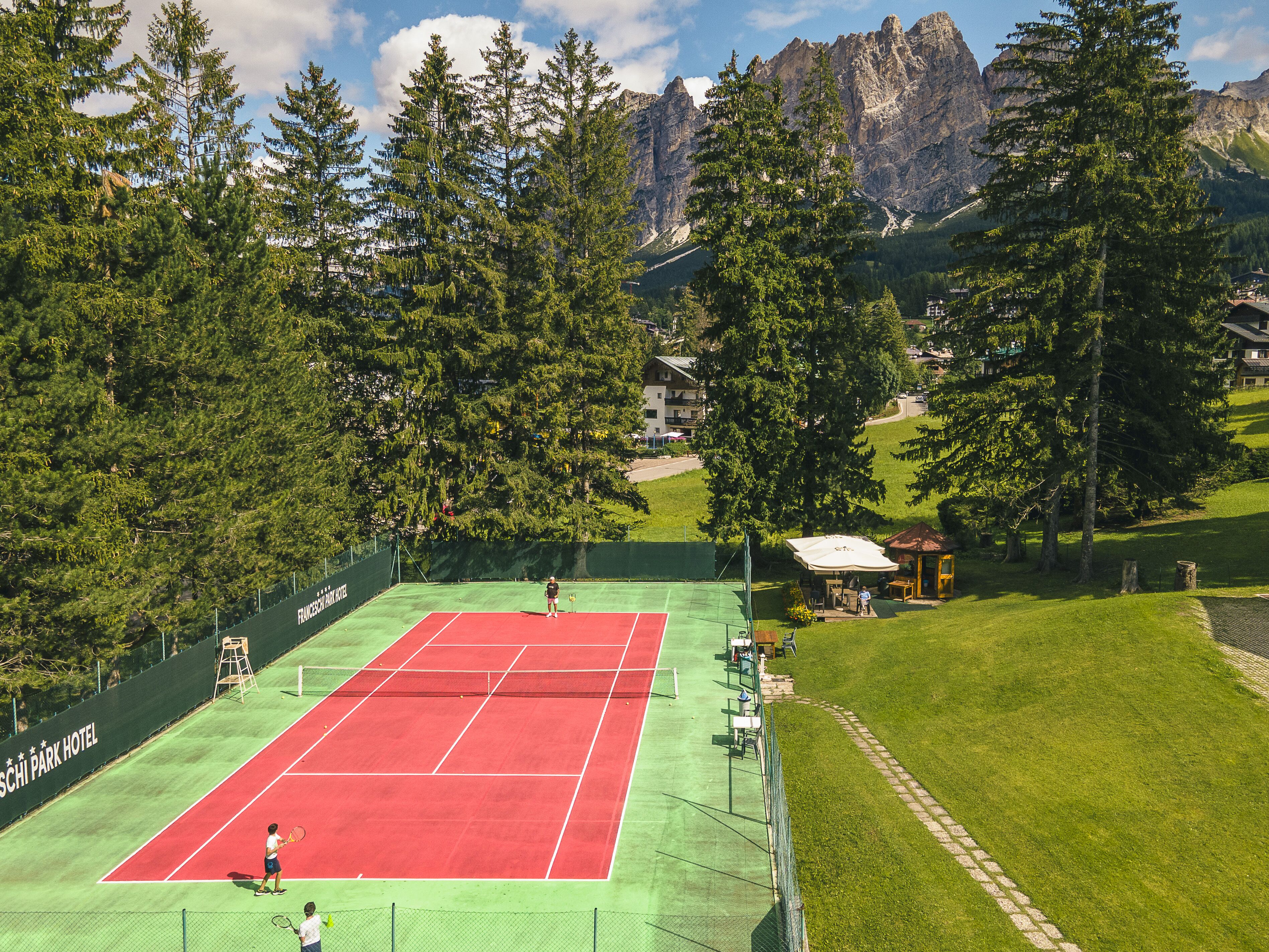 Una cancha de tenis rodeada de árboles y montañas.