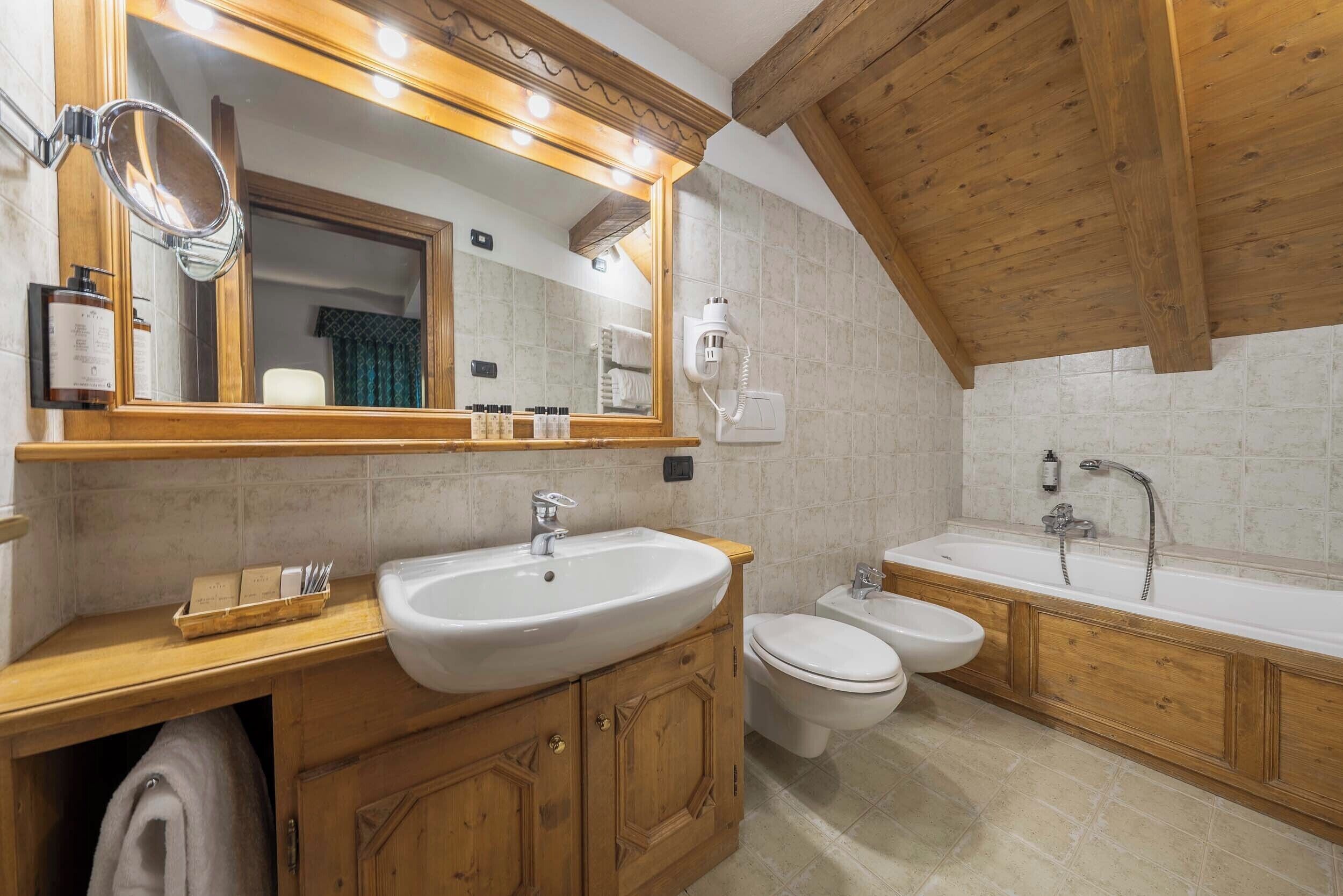 A bathroom with a wooden vanity, a large mirror, a sink, a toilet, and a bathtub.