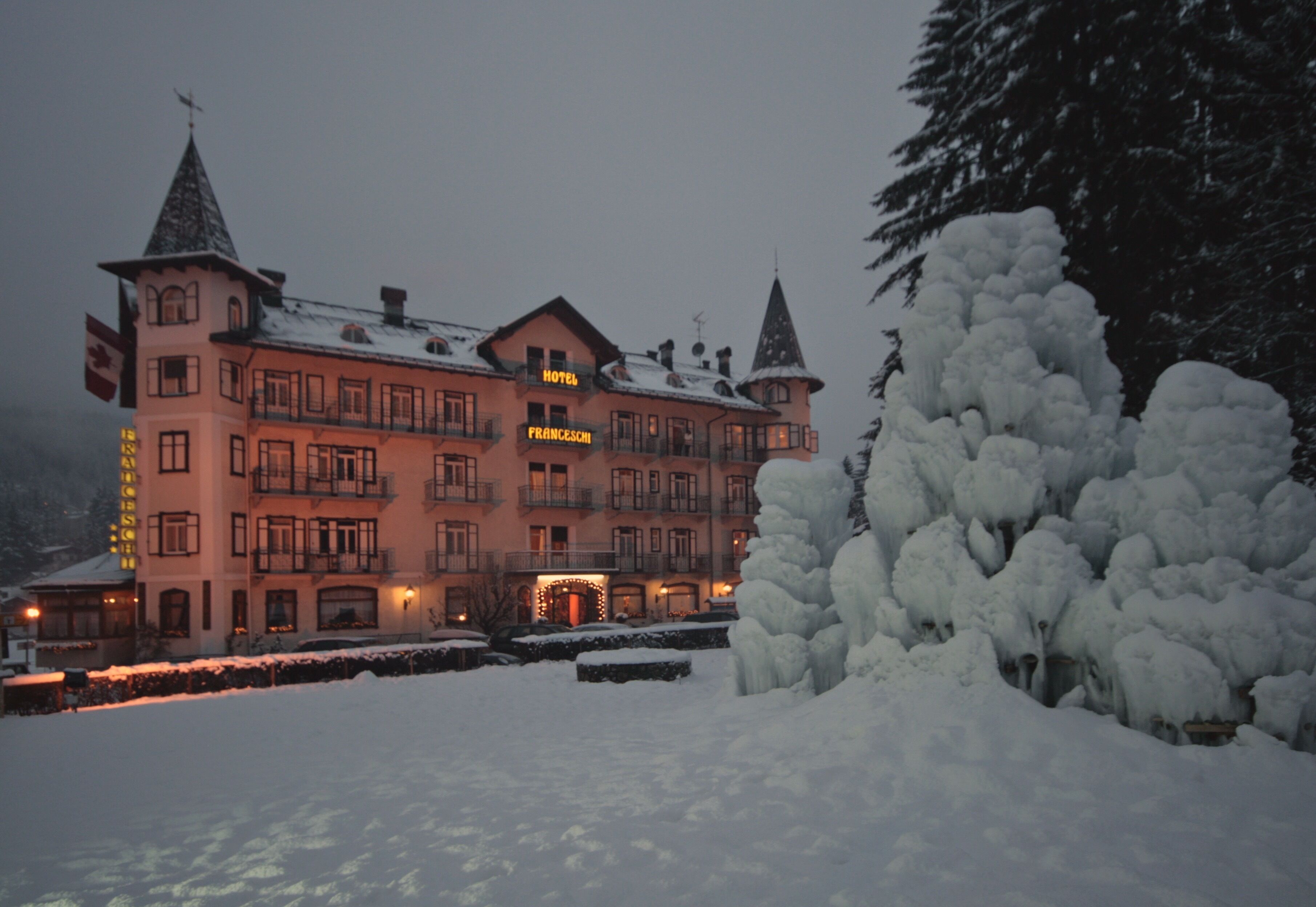 A large, multi-story hotel with a prominent "HOTEL FRANCESCH" sign, surrounded by snow-covered trees and a snow-covered lawn.