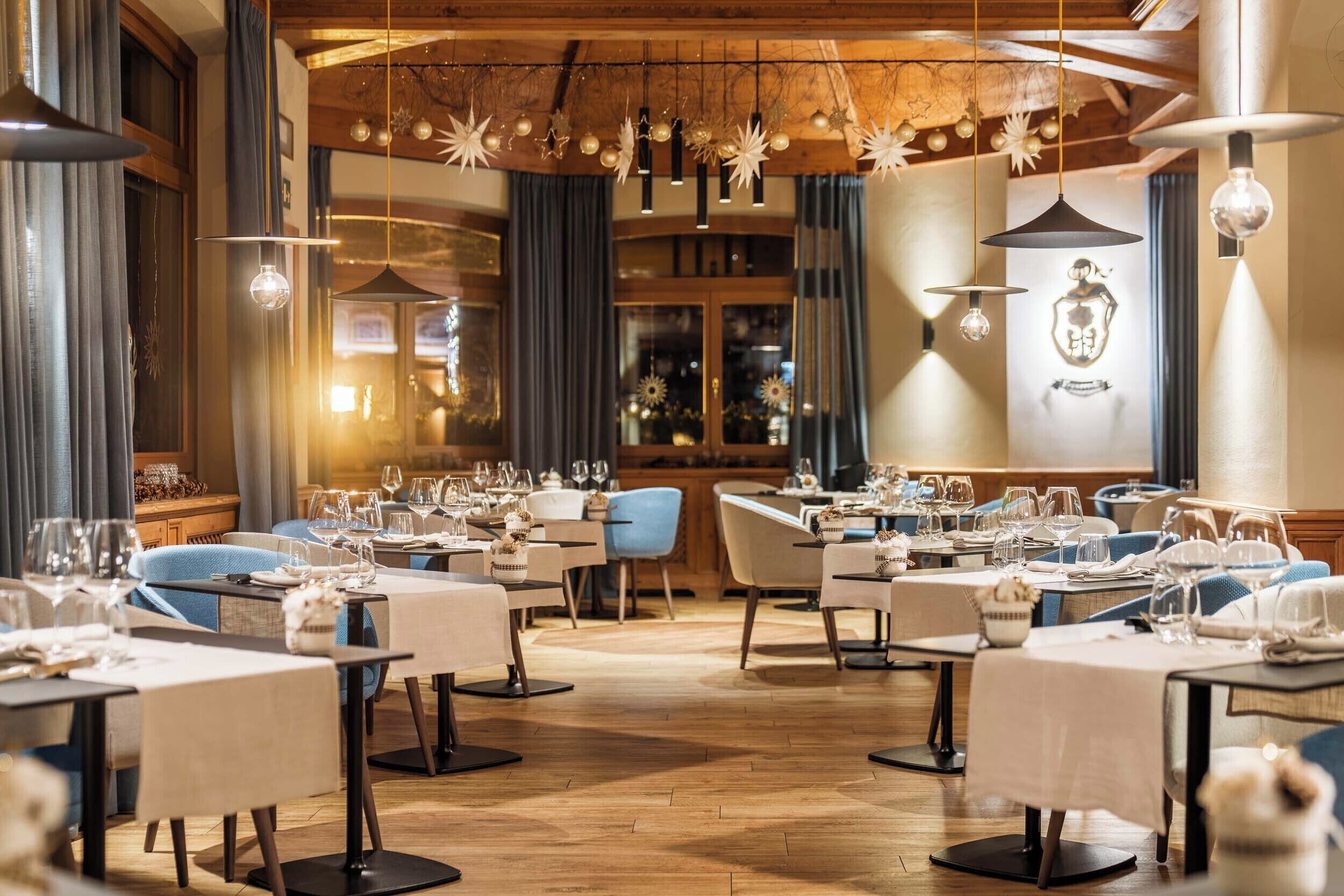 Un restaurante con varias mesas dispuestas para comer, suelos de madera y lámparas colgantes.