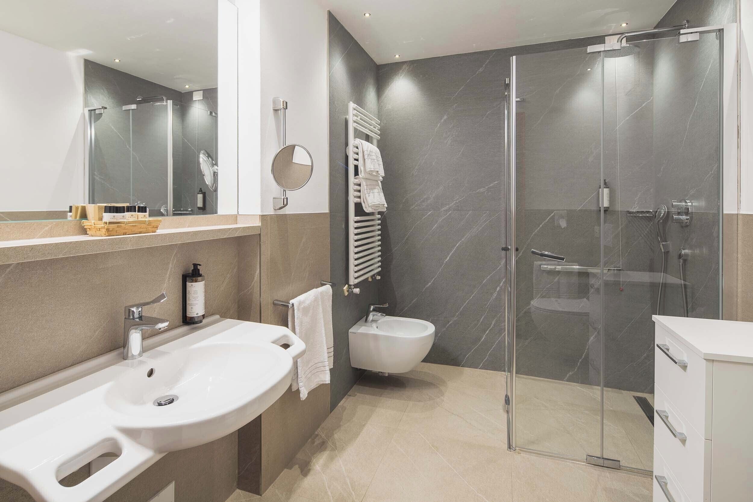Un bagno moderno con un lavandino capiente, un bidet, una cabina doccia in vetro e uno specchio.