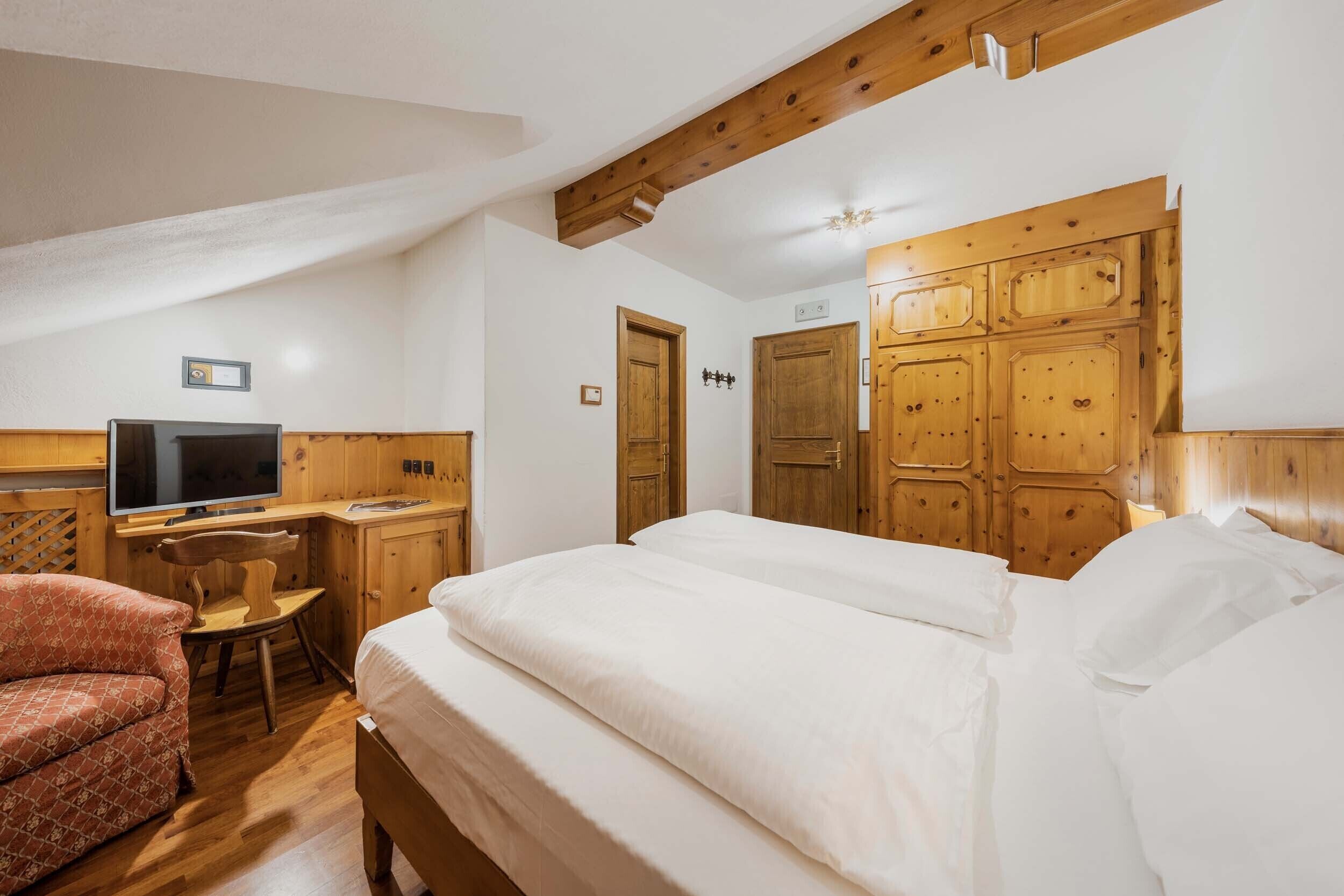 Ein Hotelzimmer mit Holzboden, einem Bett mit weißer Bettwäsche, einem Schreibtisch mit Fernseher und einem Sessel.
