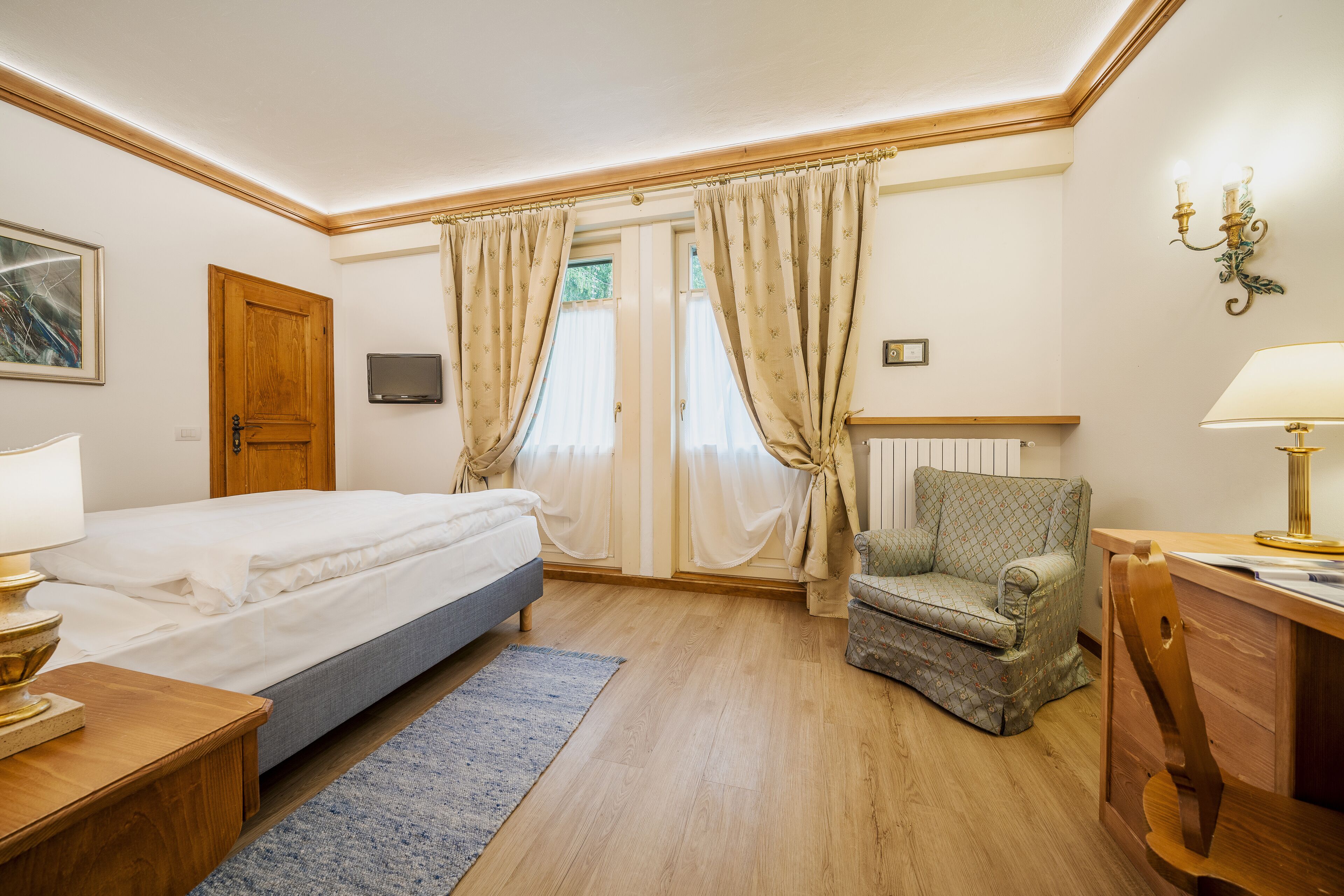 A bedroom with a bed, a chair, a desk, a lamp, a TV, and curtains.
