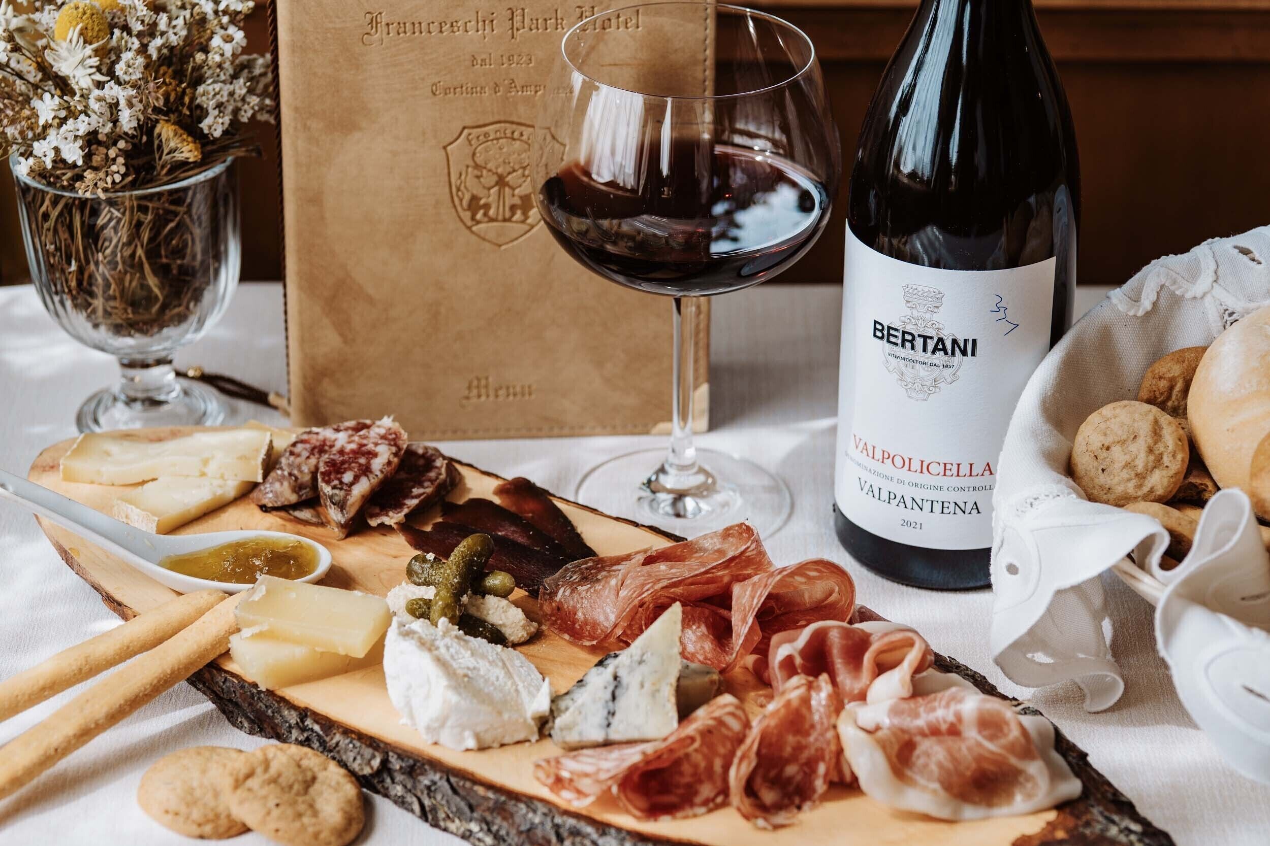 Une table garnie d’une variété de fromages, de charcuteries et de biscuits secs, une bouteille de vin et un verre de vin rouge.