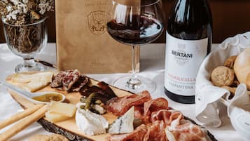 A table with a variety of cheeses, meats, and crackers, a bottle of wine, and a glass of red wine.