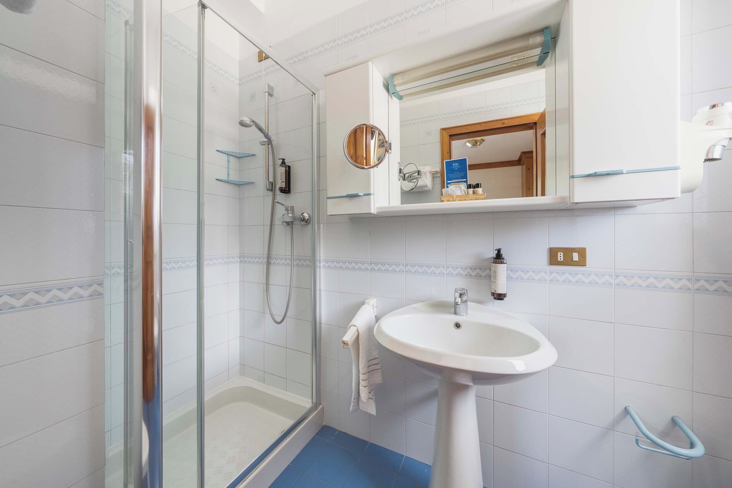 A bathroom with a glass shower enclosure, a pedestal sink, and a mirror above the sink.