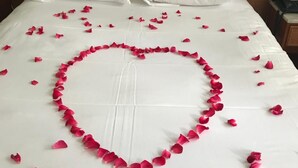 Een bed met witte lakens en een rozenblaadjesarrangement in de vorm van een hart.