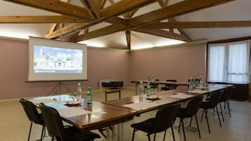 Un salón de conferencias con una larga mesa, sillas, una pantalla de proyector y un ventanal con cortinas.