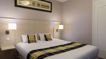 A hotel room with a large bed, two bedside lamps, a framed picture on the wall, and a door to the right.