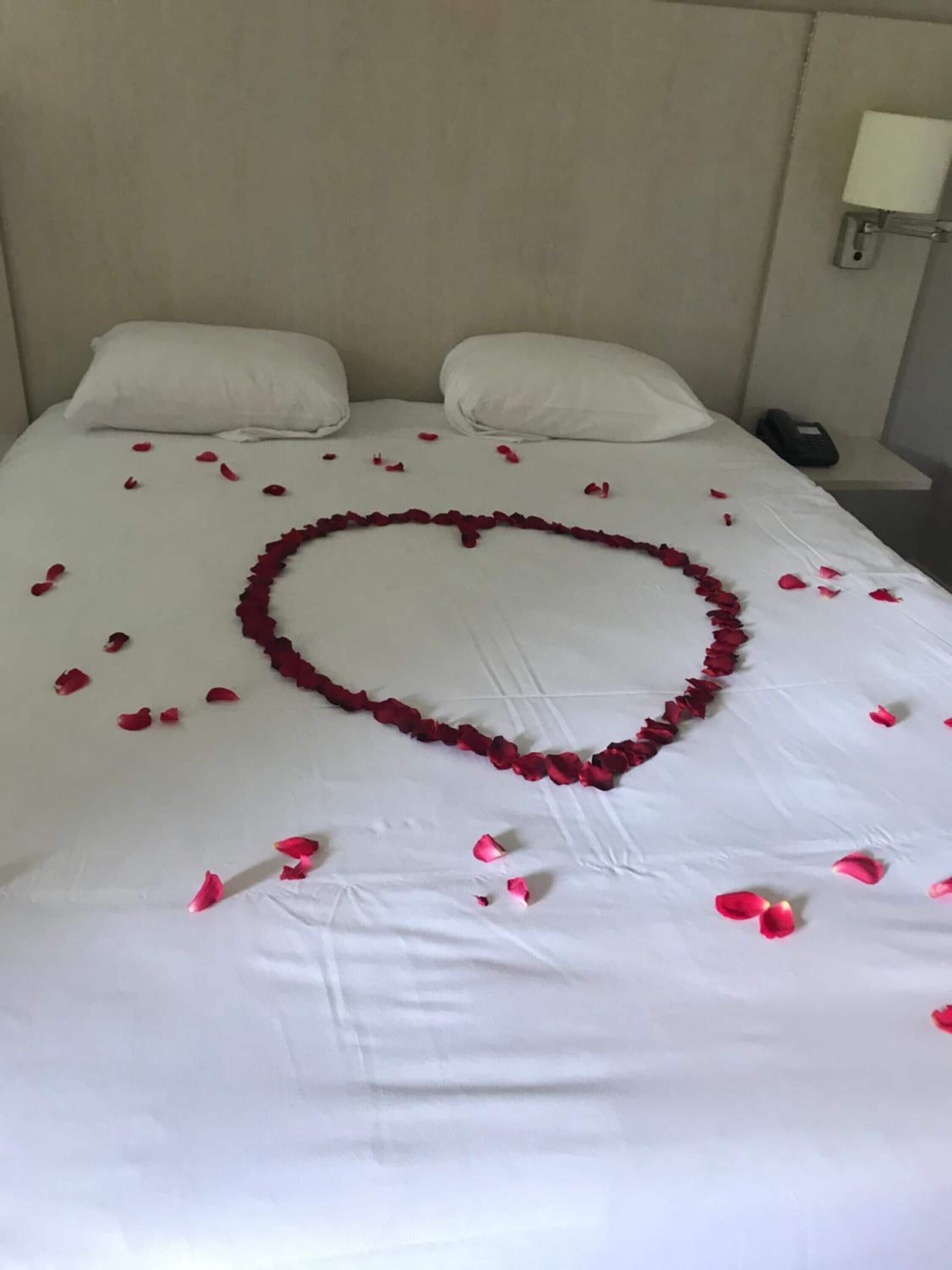 Un lit recouvert de draps blancs, et au centre, une composition en forme de cœur faite de pétales de roses.