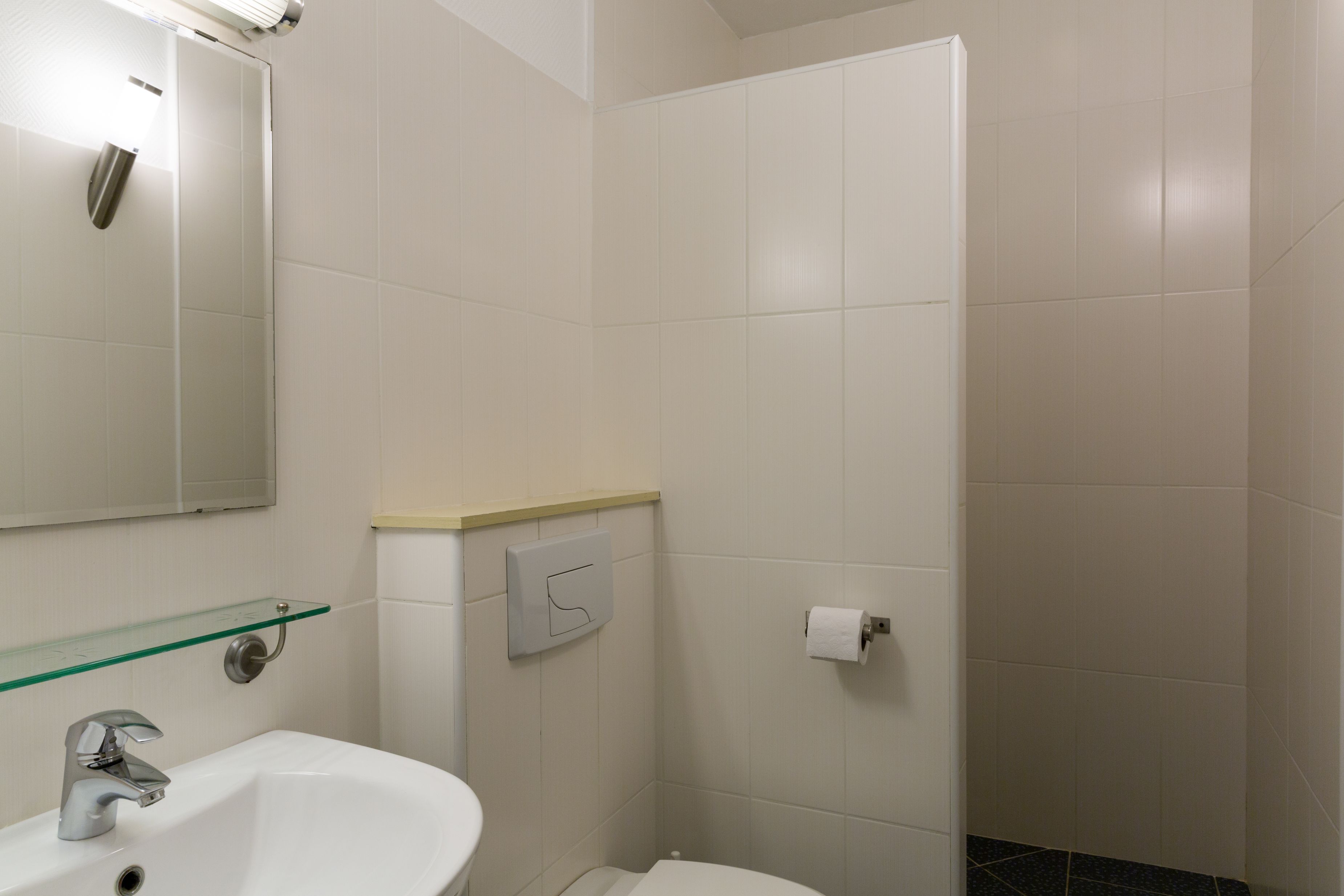 Un baño con lavamanos blanco, un espejo, repisa de vidrio, inodoro y zona de ducha.
