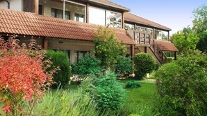 Een gebouw met twee verdiepingen, voorzien van een pannendak, omgeven door weelderige begroeiing en een verzorgde tuin.