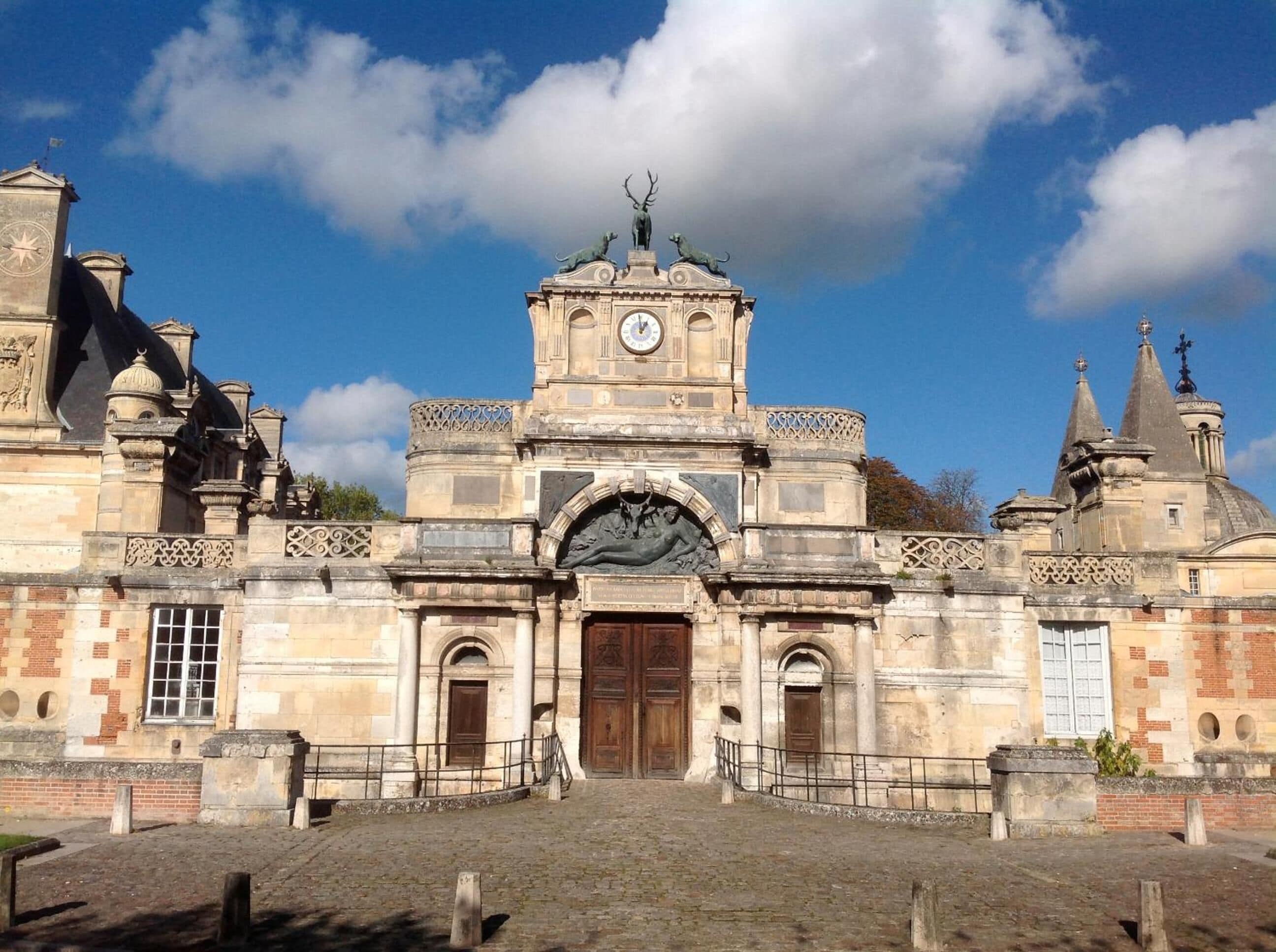 A historic building with a central clock tower, arched entrance, and statues on the roof.
