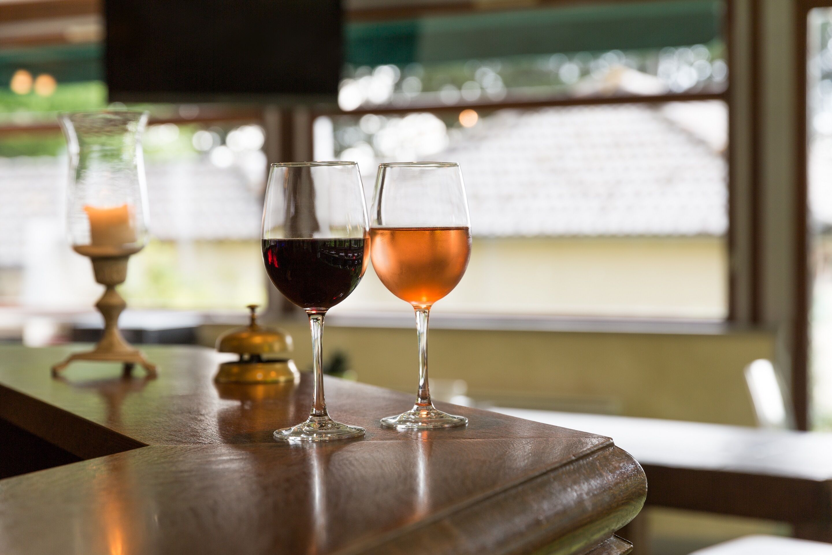 Two wine glasses on a wooden table with a candle and a bell in the background.