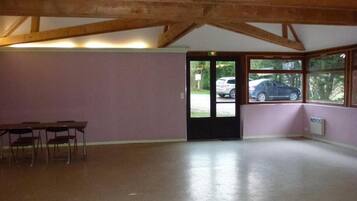 A spacious room with a high wooden ceiling, a door leading outside, and a view of parked cars through large windows.