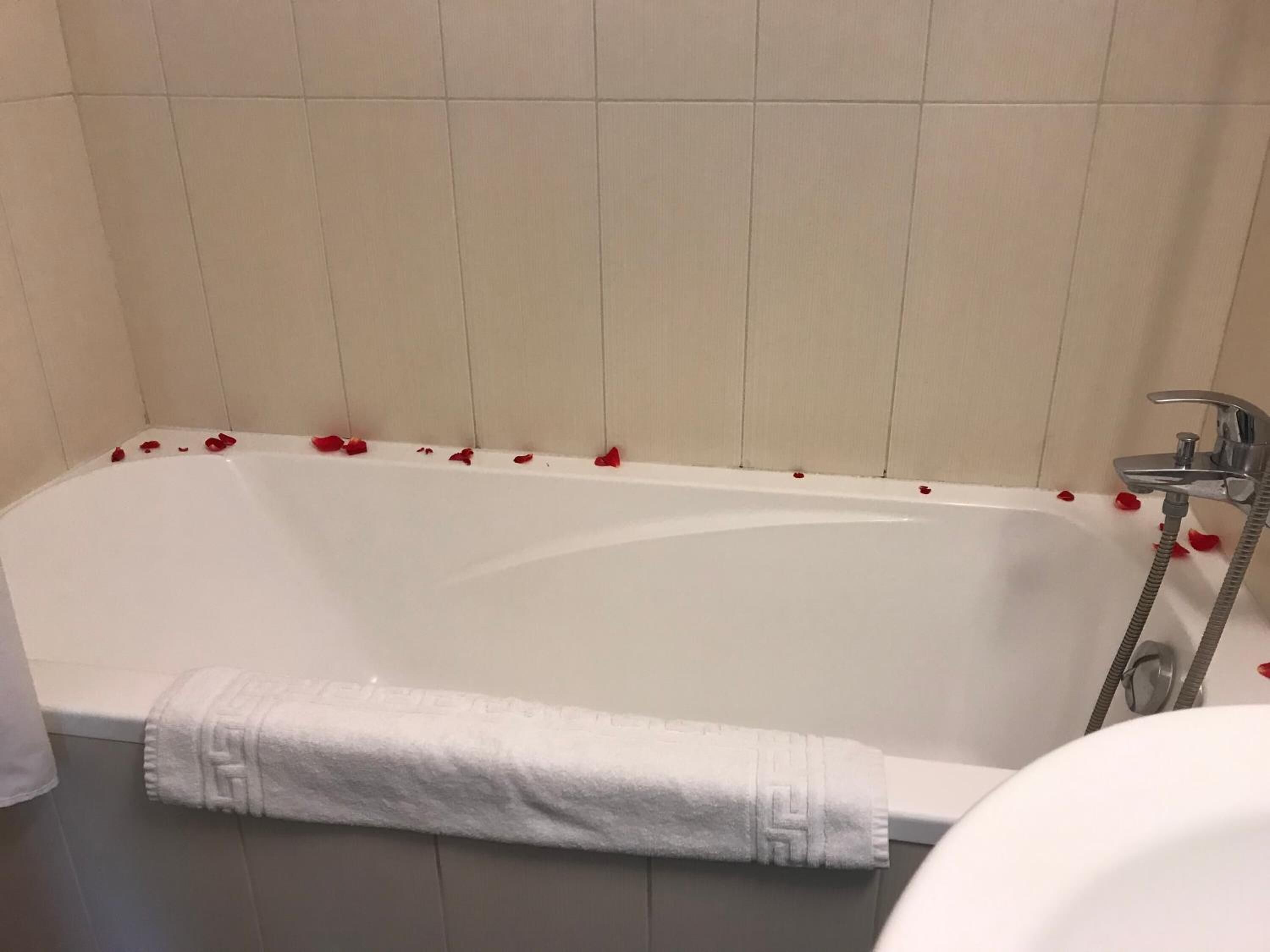 Eine Wanne mit Rosenblüten, ein weißes Handtuch und eine Duschbrause.