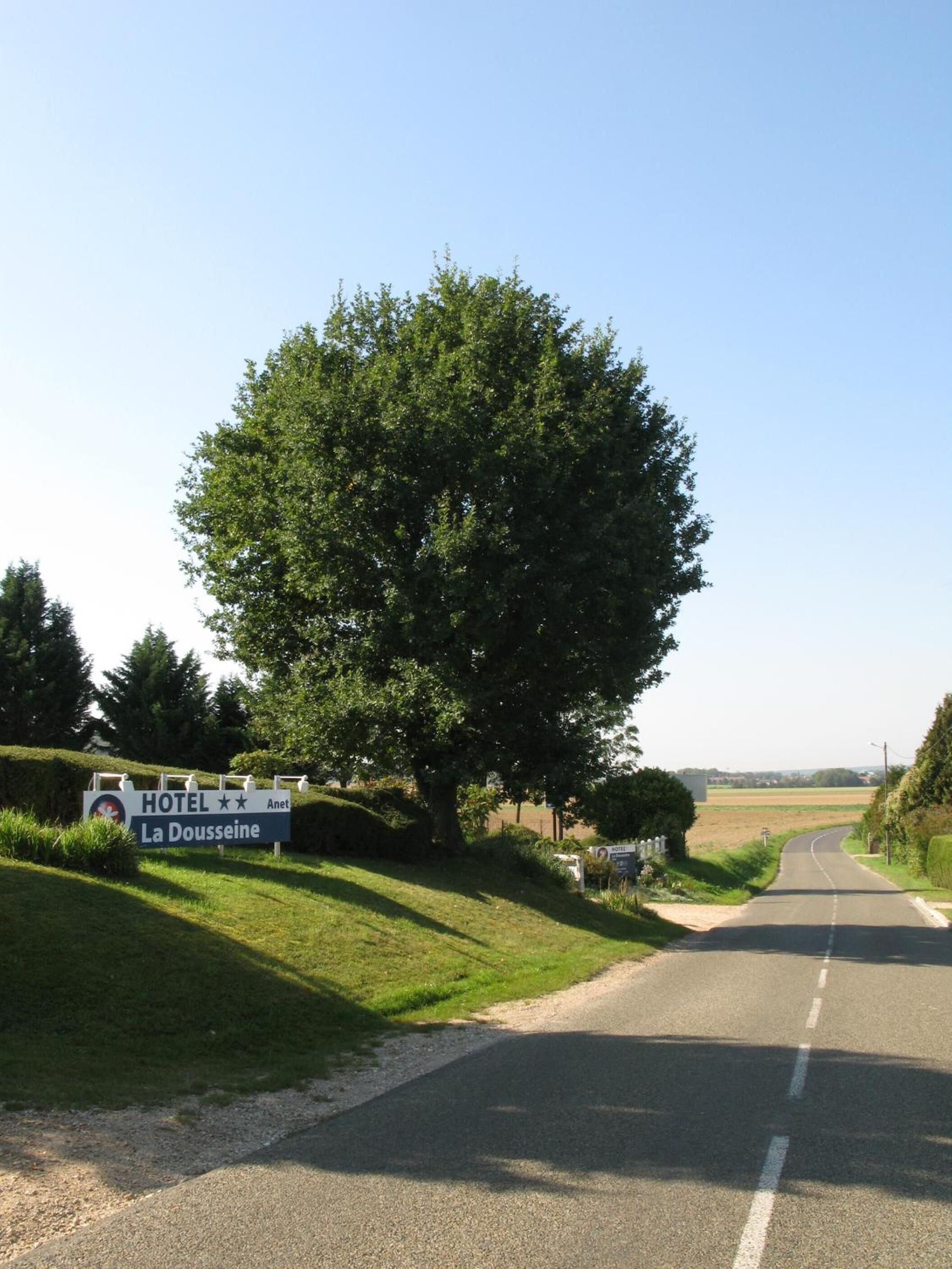 A road leading to a hotel named 'La Doussieine' with a large tree on the left.