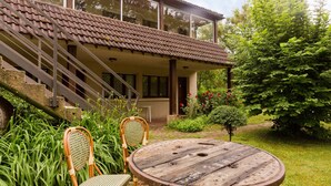 Een huis met een terras, twee rieten stoelen en een ronde houten tafel.