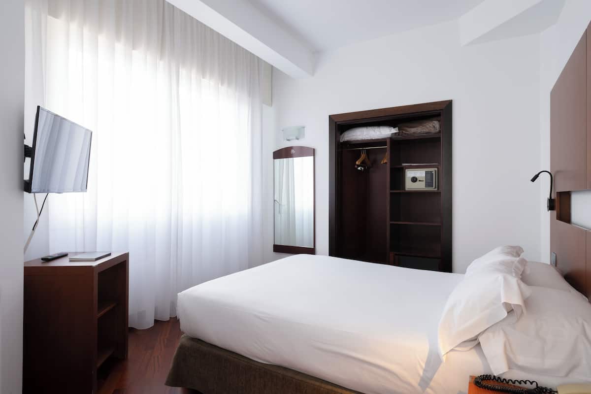 Una habitación de hotel con una cama, televisión, armario y espejo.