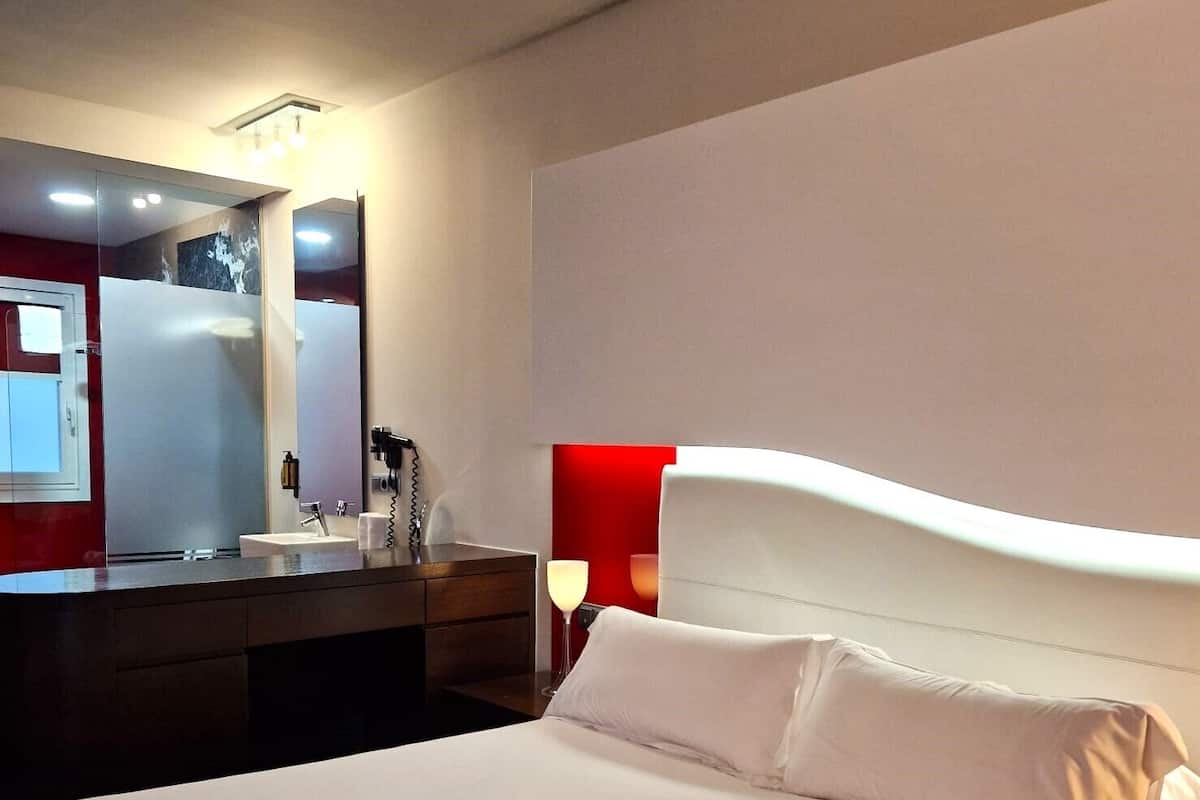 Una habitación de hotel con una cama grande, una mesita de noche, un espejo y una pared de acento roja.