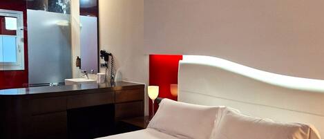 A hotel room with a large bed, a bedside table, a mirror, and a red accent wall.