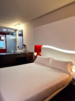 A hotel room with a large bed, a bedside table, a mirror, and a red accent wall.