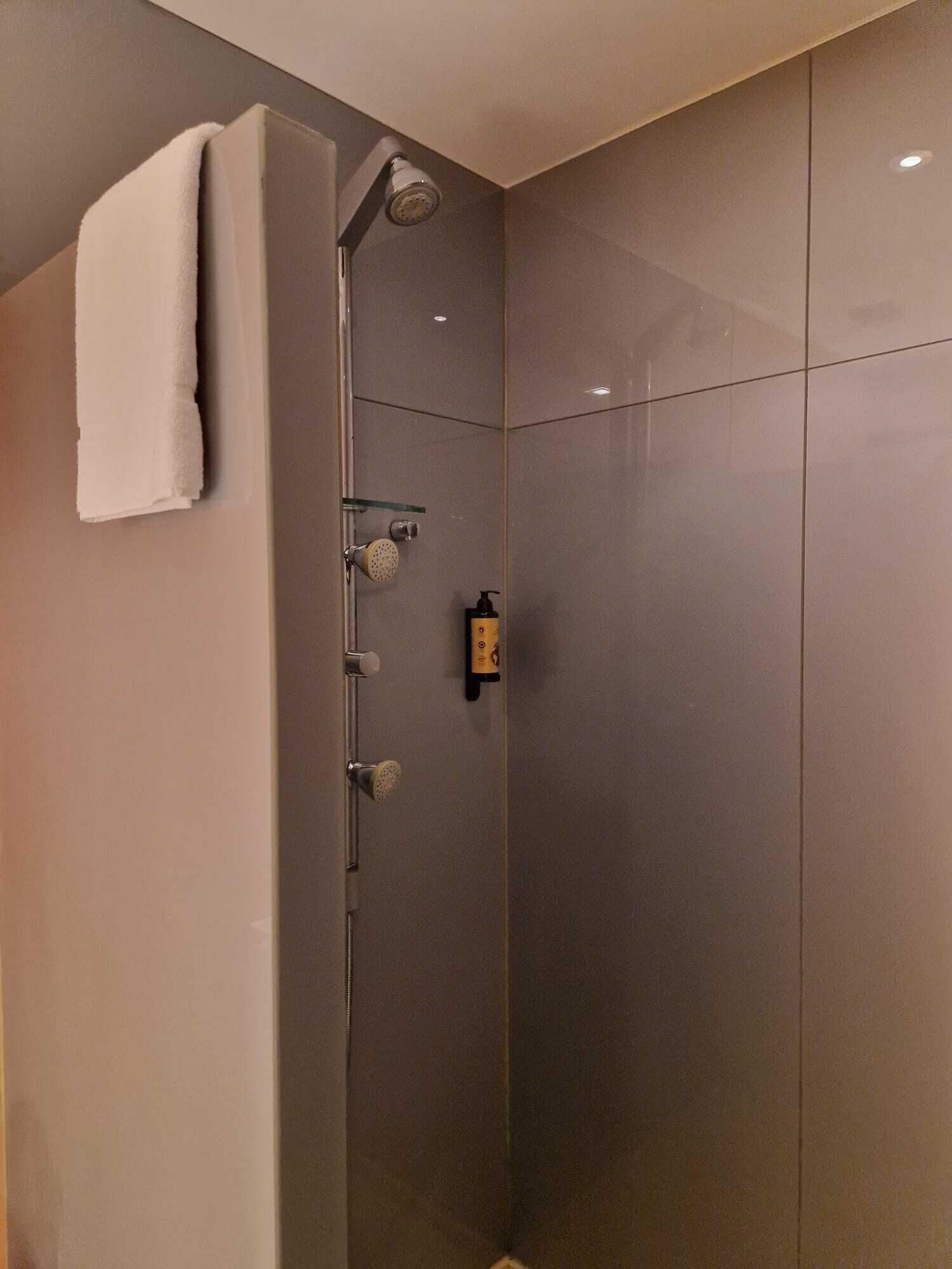 Una ducha moderna con puerta de vidrio, una toalla colgada en la pared y un dispensador de jabón.