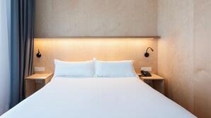 Una cama bien hecha con sábanas blancas, dos mesitas de noche con lámparas y un cabecero de madera.