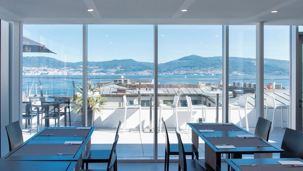 Una sala de reuniones moderna con amplios ventanales que ofrecen vistas panorámicas del mar y del paisaje urbano.