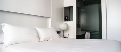Une chambre d’hôtel moderne avec un grand lit, un luminaire rond fixé au mur et une salle de bain visible avec un miroir.