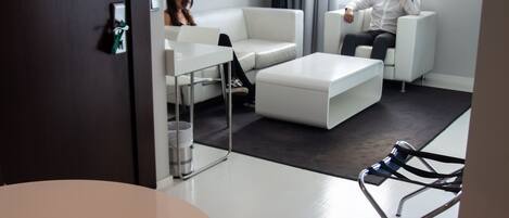 A modern hotel room with a white sofa, a round table, and a glass chair.