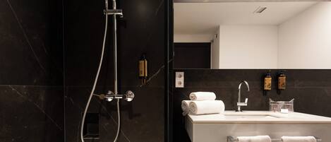 A modern bathroom with a dark marble wall, a shower with a handheld hose, a sink with a mirror, and two bottles of soap.