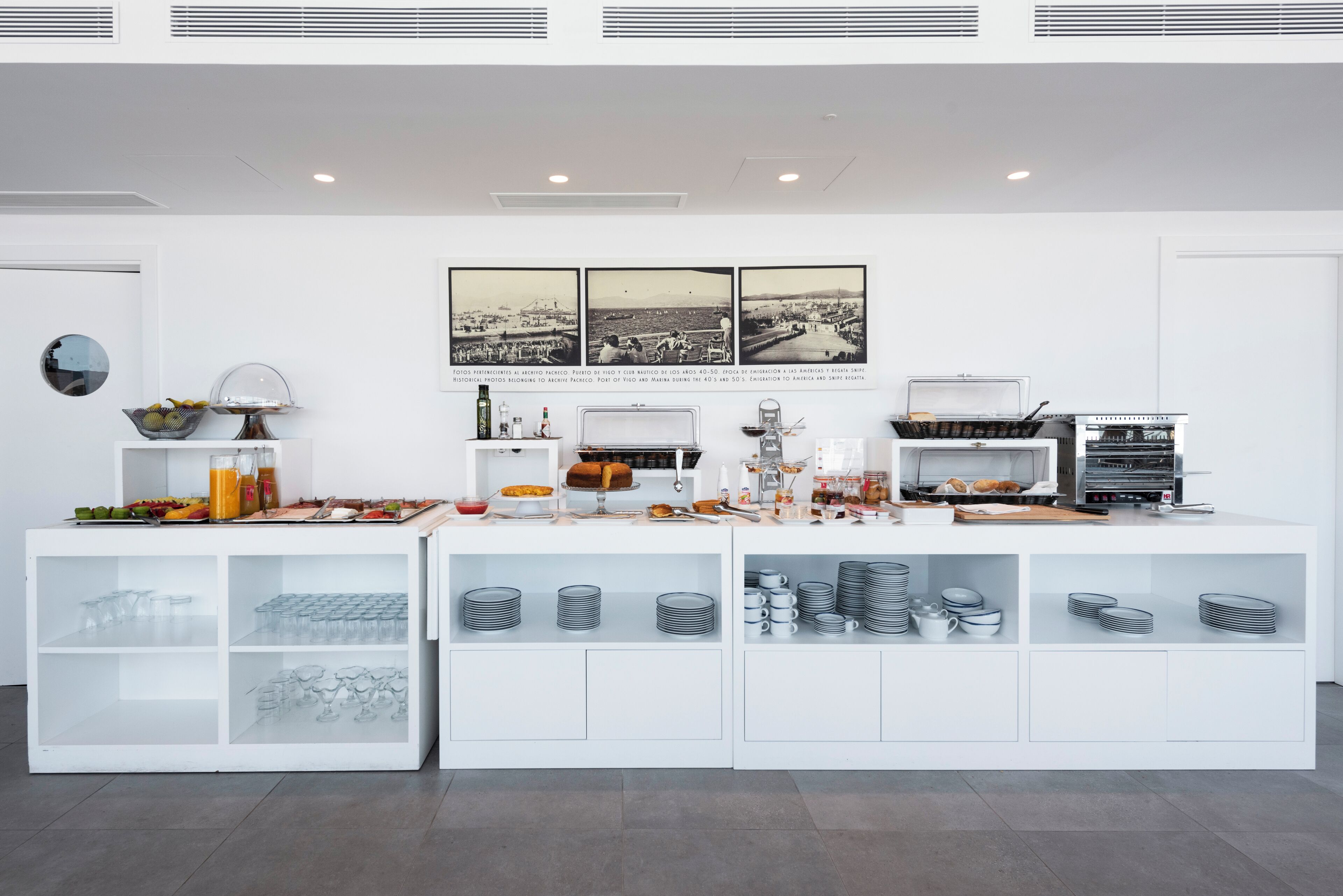 Un bar à petit-déjeuner moderne au design épuré, proposant une variété d'aliments et de boissons, notamment des fruits, des viennoiseries et des boissons diverses.