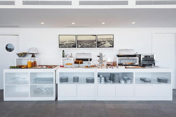 A modern breakfast bar with a white design, featuring a variety of food and drink options, including fruits, pastries, and beverages.