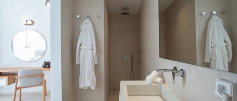 A modern bathroom with a large mirror, a shower, and a vanity with toiletries.