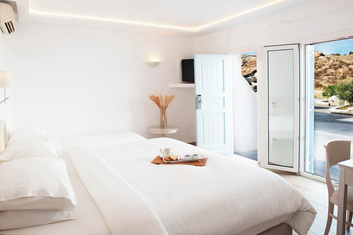 Moderni hotellihuone, jossa on suuri sänky, aamiaistarjotin, hyllyllä oleva televisio ja näkymä ulos.